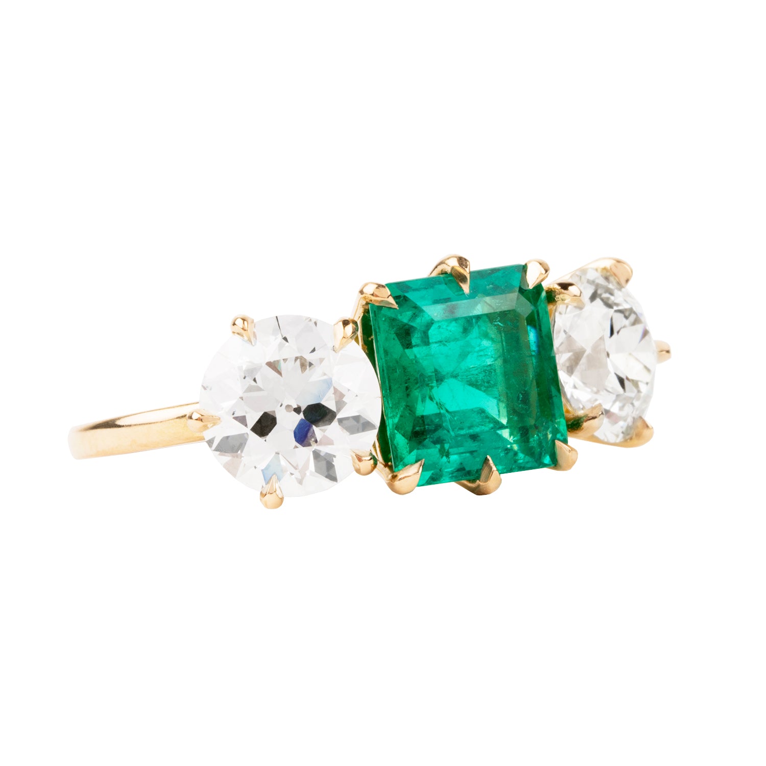 A three-stone emerald and diamond ring with a slim band, featuring a central emerald stone surrounded by two diamond side stones, all set in 18k old gold.