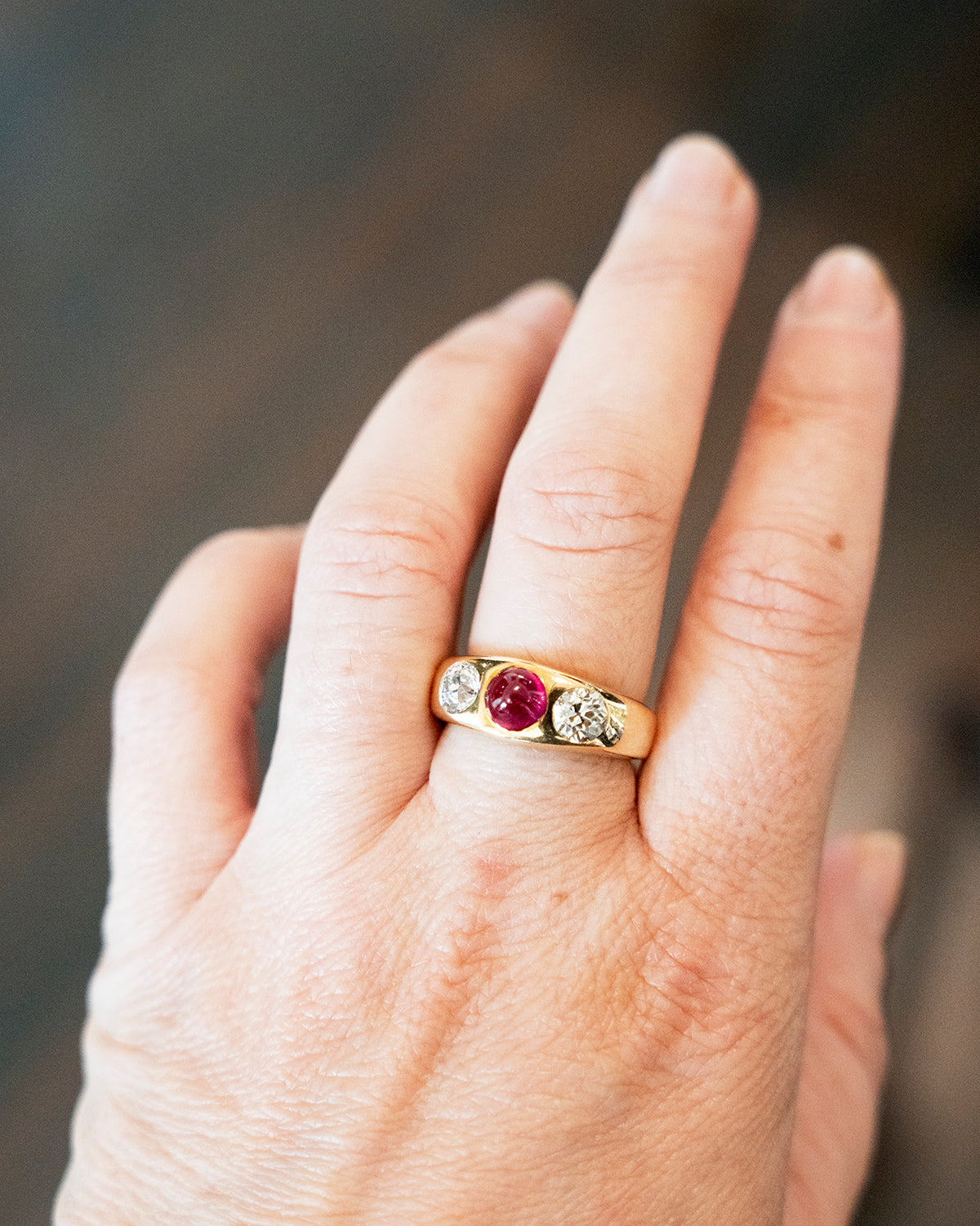 Early 20th century ruby and diamond three stone ring. In a flush 18k gold setting. Two old European cut diamonds flank a bright Burmese ruby cabochon with a high dome. English in origin. Circa 1910. Model view of the ring being worn for scale.