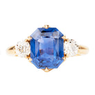 A three-stone ring with a large blue sapphire centerpiece and two smaller old European cut diamonds, all set in a gold band.