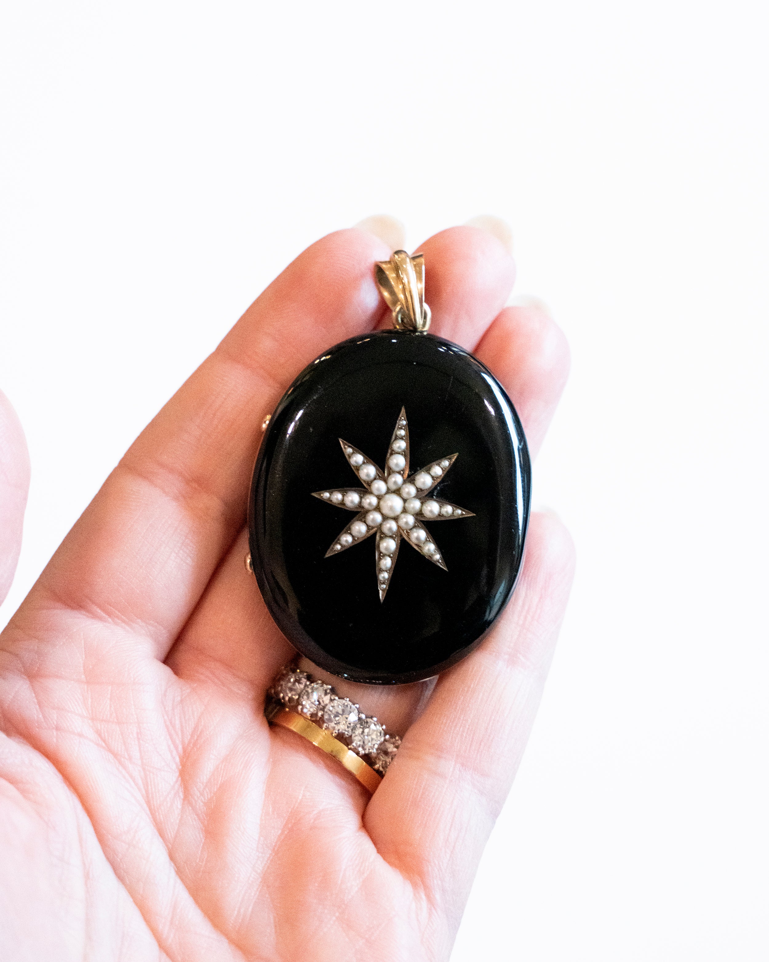 A bold black enamel locket with a pearl starburst motif. The locket is crafted in 18k gold. It opens to reveal two compartments for photographs or keepsakes. England, circa 1870.