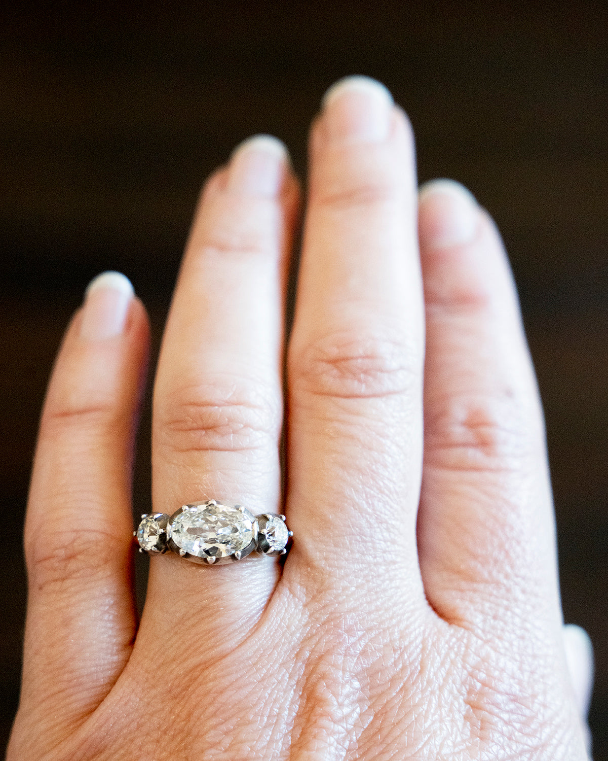 One of our signature designs, in silver-topped 18k gold. This design s inspired by a labor-intensive setting technique common in 18th and 19th-century rings. The silver-on-gold technique is true to the rings that inspired this design and is rarely seen in modern jewelry. This ring features a GIA certified cushion cut diamond, 1.58 carat, I color and VS2 clarity. The center stone is paired with approximately .30 carat and .28 carat I color and VS2 clarity old mine cut diamonds. The ring being worn on a hand.