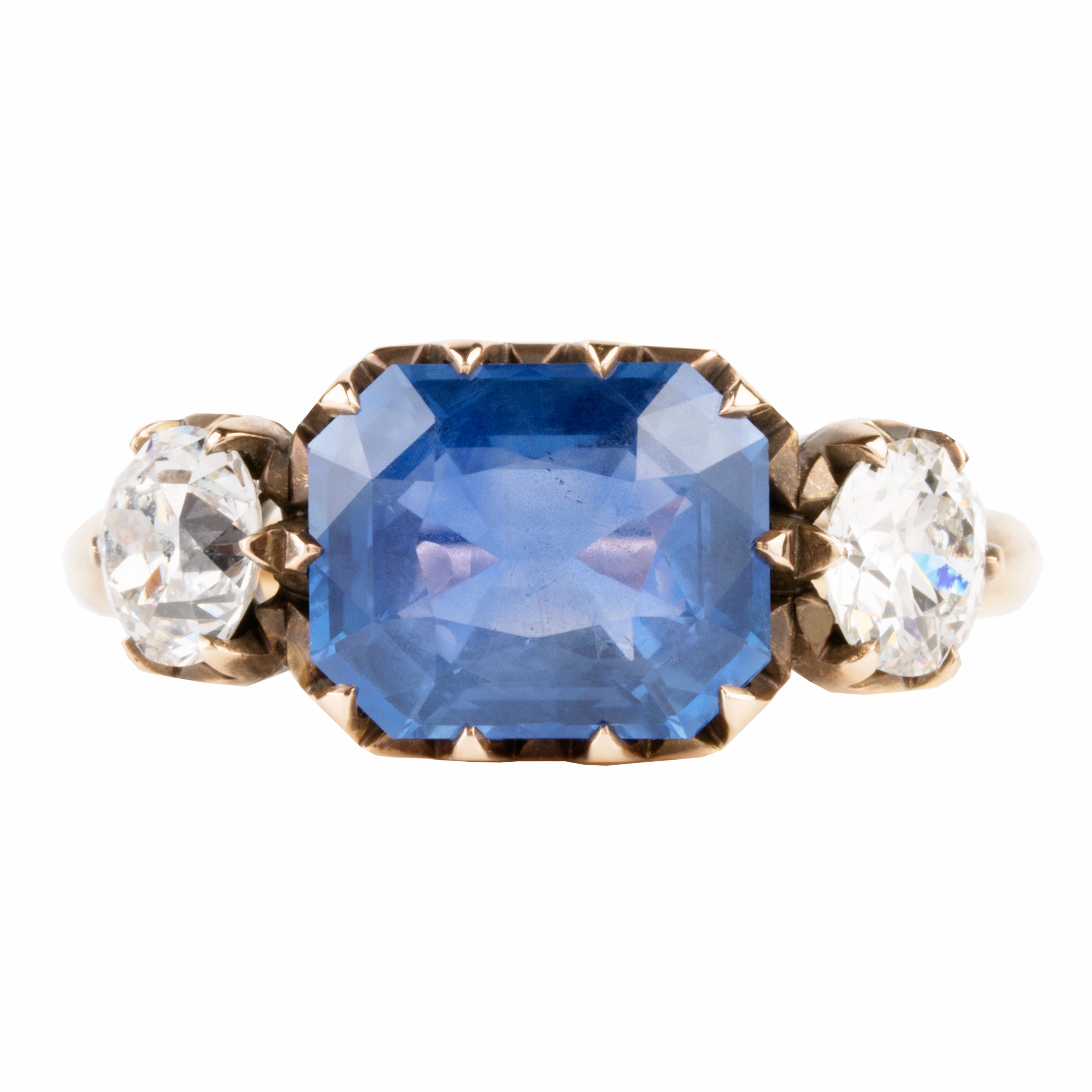 A three stone old mine cut diamond ring with a large blue sapphire center stone and two smaller old European cut side diamonds, all in a rose gold band.
