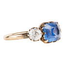 A three stone old mine cut diamond ring with a large blue sapphire center stone and two smaller old European cut side diamonds, all in a rose gold band.
