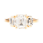 A hand fabricated 18k old gold emerald cut diamond ring with four tab prongs and two emerald cut side stones, featuring a squared off band.
