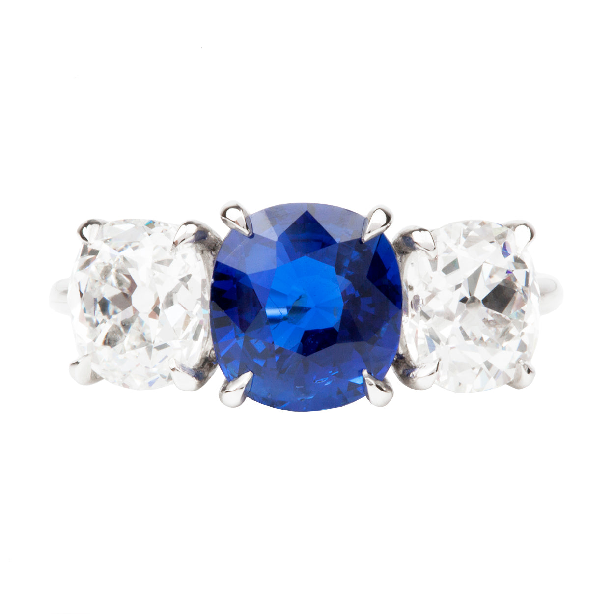 A classic three stone diamond ring with a cushion cut sapphire center stone and two old mine cut diamond side stones, all set in a platinum band.