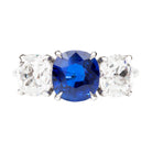A classic three stone diamond ring with a cushion cut sapphire center stone and two old mine cut diamond side stones, all set in a platinum band.