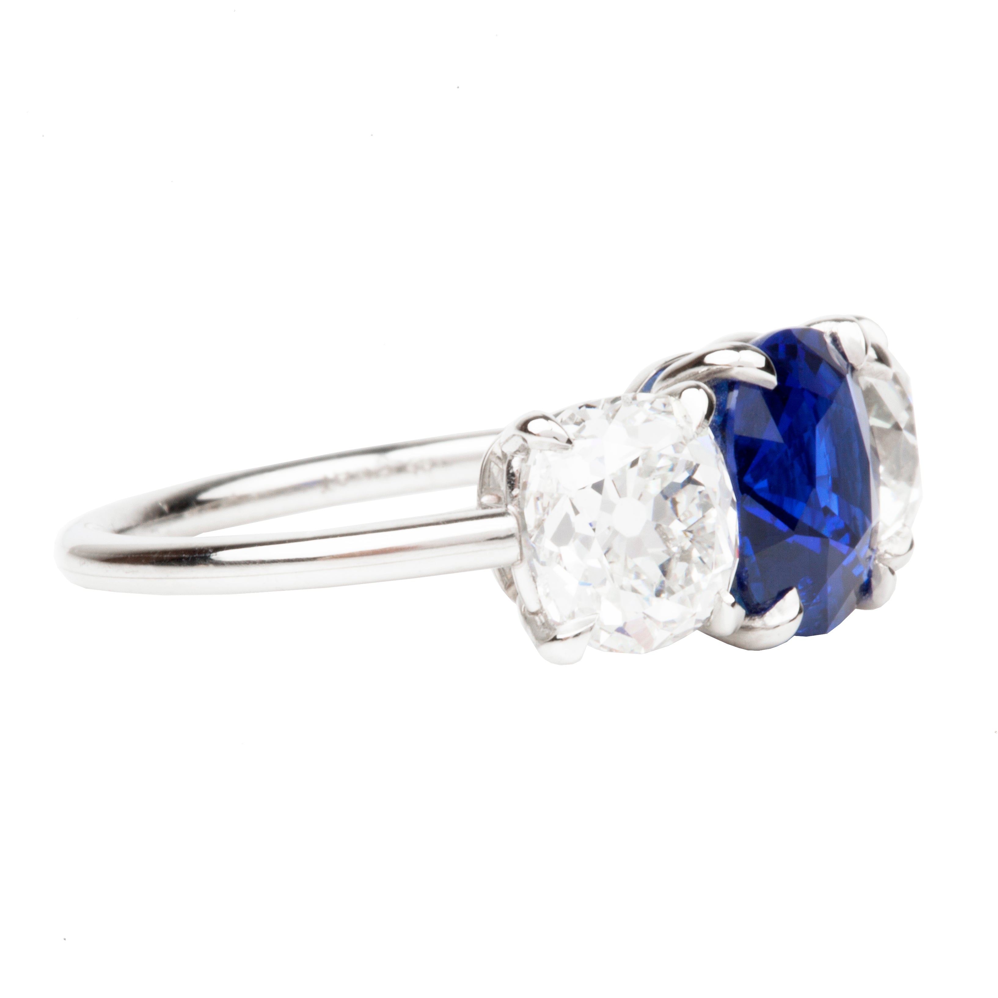 A classic three stone diamond ring with a cushion cut sapphire center stone and two old mine cut diamond side stones, all set in a platinum band.