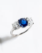 A classic three stone diamond ring with a cushion cut sapphire center stone and two old mine cut diamond side stones, all set in a platinum band.