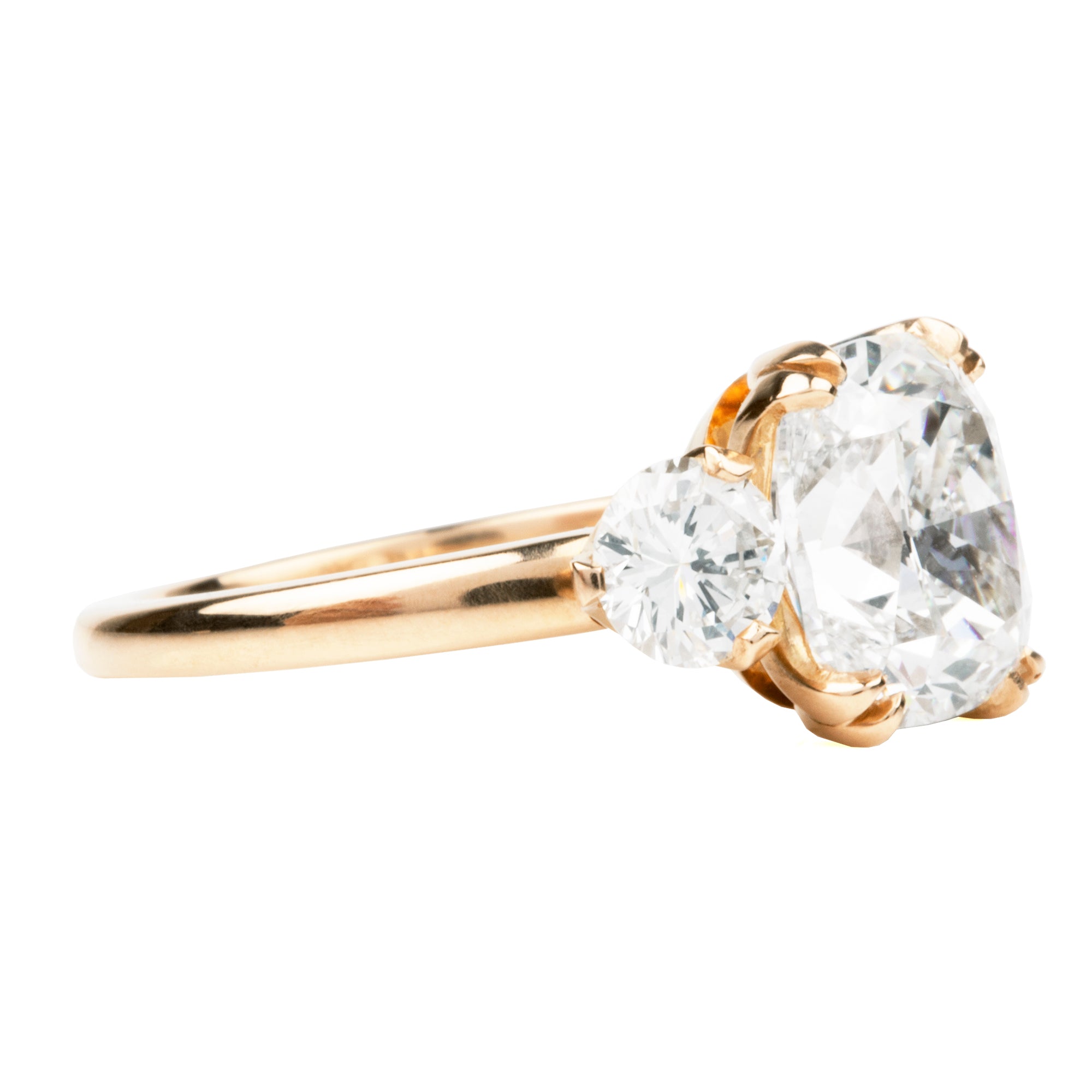 A classic three stone ring with a central cushion cut diamond and two round brilliant cut diamonds, handcrafted in 18k old gold with a simple band.