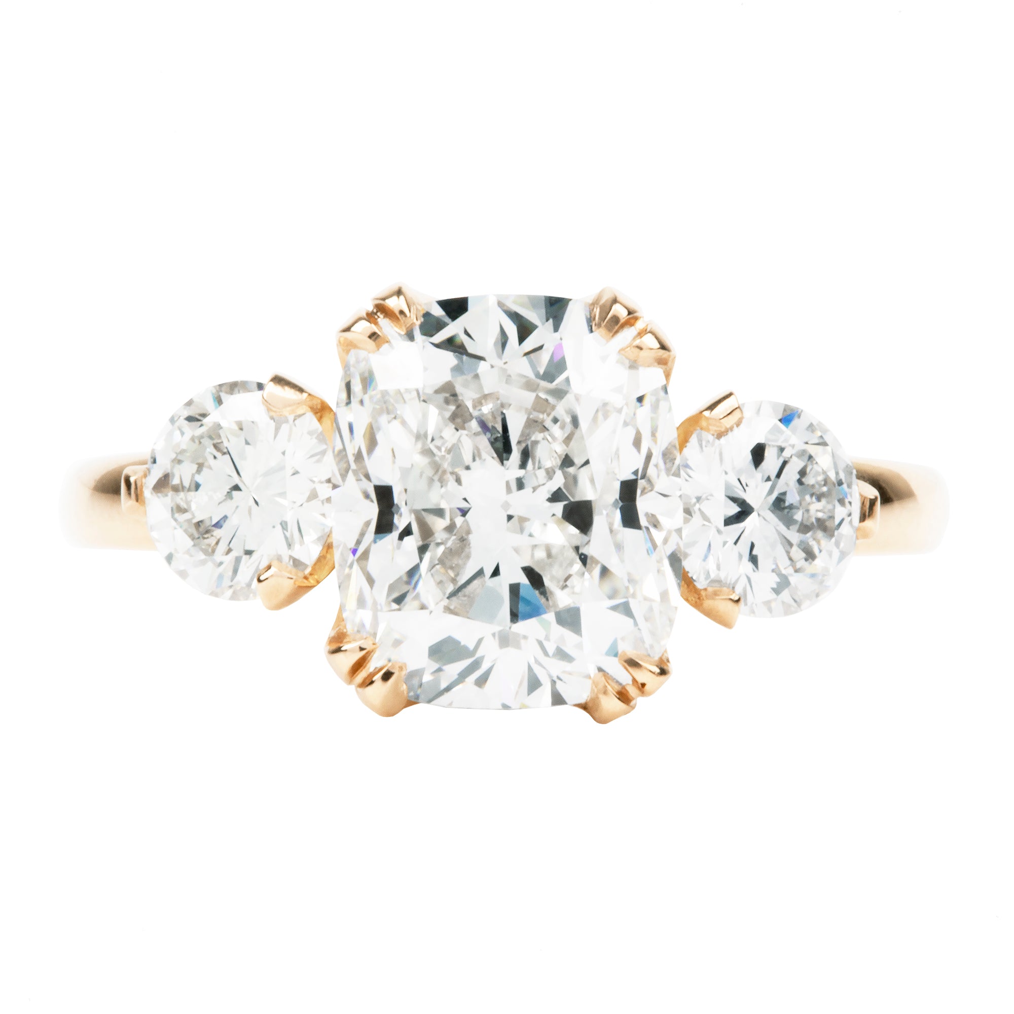 A classic three stone ring with a central cushion cut diamond and two round brilliant cut diamonds, handcrafted in 18k old gold with a simple band.