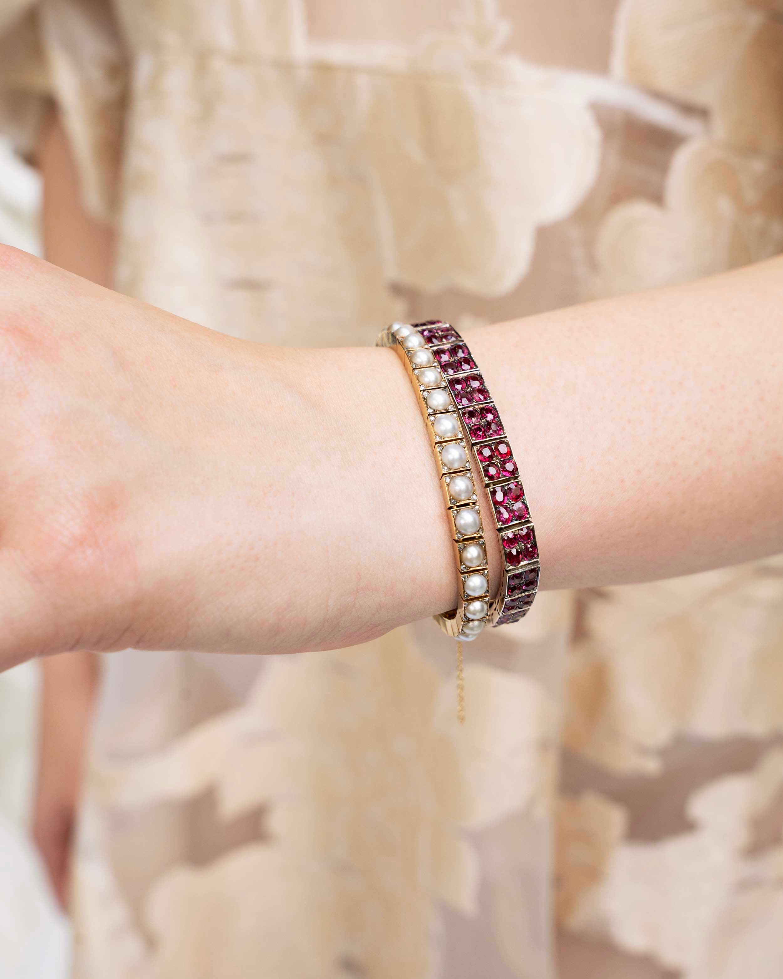 Edwardian era pearl and diamond line bracelet. White split pearls are set in 18k yellow gold. Each pearl is pointed with four rose cut diamonds in square settings. England, circa 1910. Model wearing the pearl bracelet along with a ruby line bracelet. 