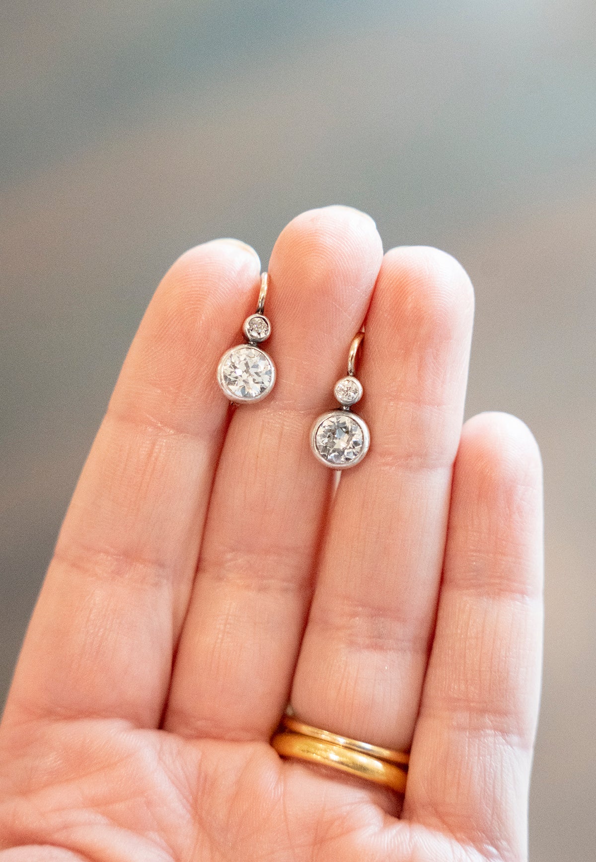 Antique old European cut diamond two-stone earrings. Set in bezel set Silver topped 14k gold. A hand engraved detail on each hook reads "2.75" which is the estimated total diamond weight.The stones are estimated to be J-L in color and I1 in clarity. Front view. In a hand. 