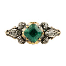 An antique-style ring featuring a central green emerald-cut gemstone flanked by small clear stones in a gold-toned setting, with a silver-toned band decorated with four small round diamonds.