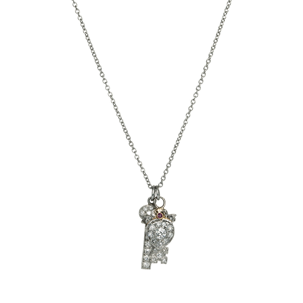 Diminutive Art Deco era ‘Key to my Heart’ charms on a platinum 18” cable link chain. A tiny heart crowned with a bow and ruby stone hanging with a matched key in platinum set with diamonds. Both pieces came from an early 20th-century charm bracelet. Continental European, 1930. Front view. 