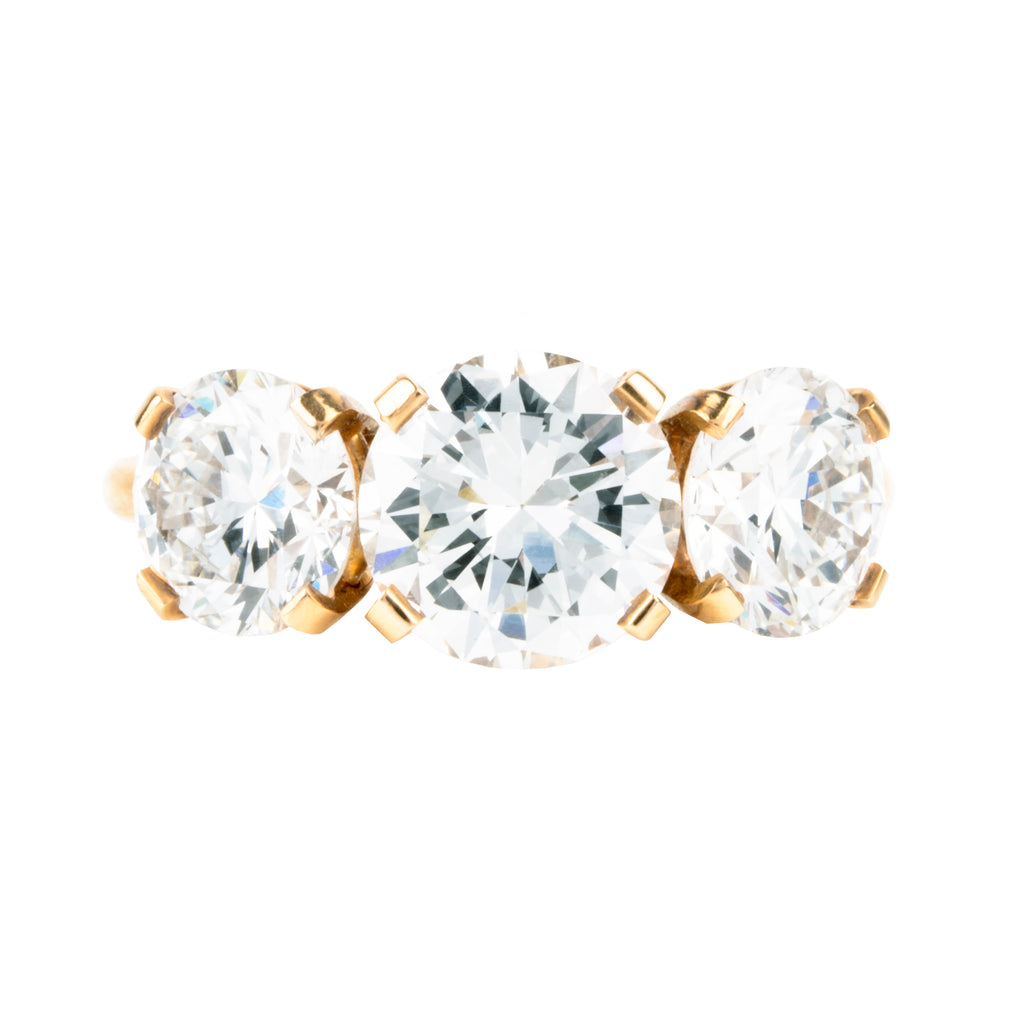 A classic three-stone diamond ring in our 18k old gold featuring a slim band. The center stone is set with four tab prongs. This example features three round brilliant cut diamonds. The center stone in this example is 1.81 carat diamond, GIA-certified H color, and VS1 clarity. Flanked by 2 GIA-certified round brilliant cut diamond side stones, 1.11 G/SI2 and 1.22 carats, F/SI1. Made in 18k old gold. Front view. 