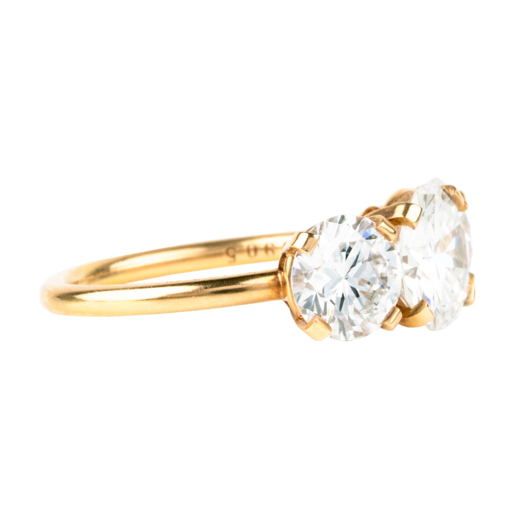 A classic three-stone diamond ring in our 18k old gold featuring a slim band. The center stone is set with four tab prongs. This example features three round brilliant cut diamonds. The center stone in this example is 1.81 carat diamond, GIA-certified H color, and VS1 clarity. Flanked by 2 GIA-certified round brilliant cut diamond side stones, 1.11 G/SI2 and 1.22 carats, F/SI1. Made in 18k old gold. Side view. 