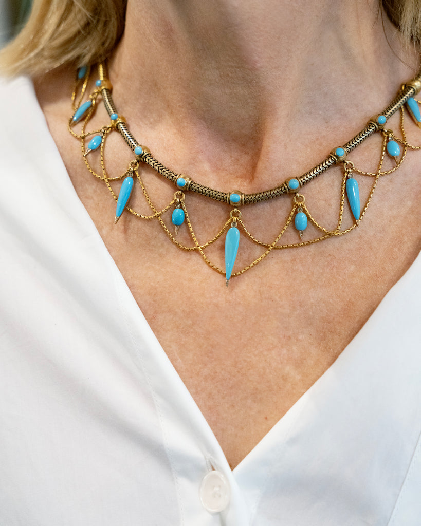 This is a rare example of an elaborate 19th-century collar necklace. Natural Persian turquoise stones are cut in the shapes of amphoras, with rose-cut diamonds set at the sharp tip of every setting. The necklace is made of 18k gold and was made in England, circa 1860. The necklace is being modeled with a white top. 
