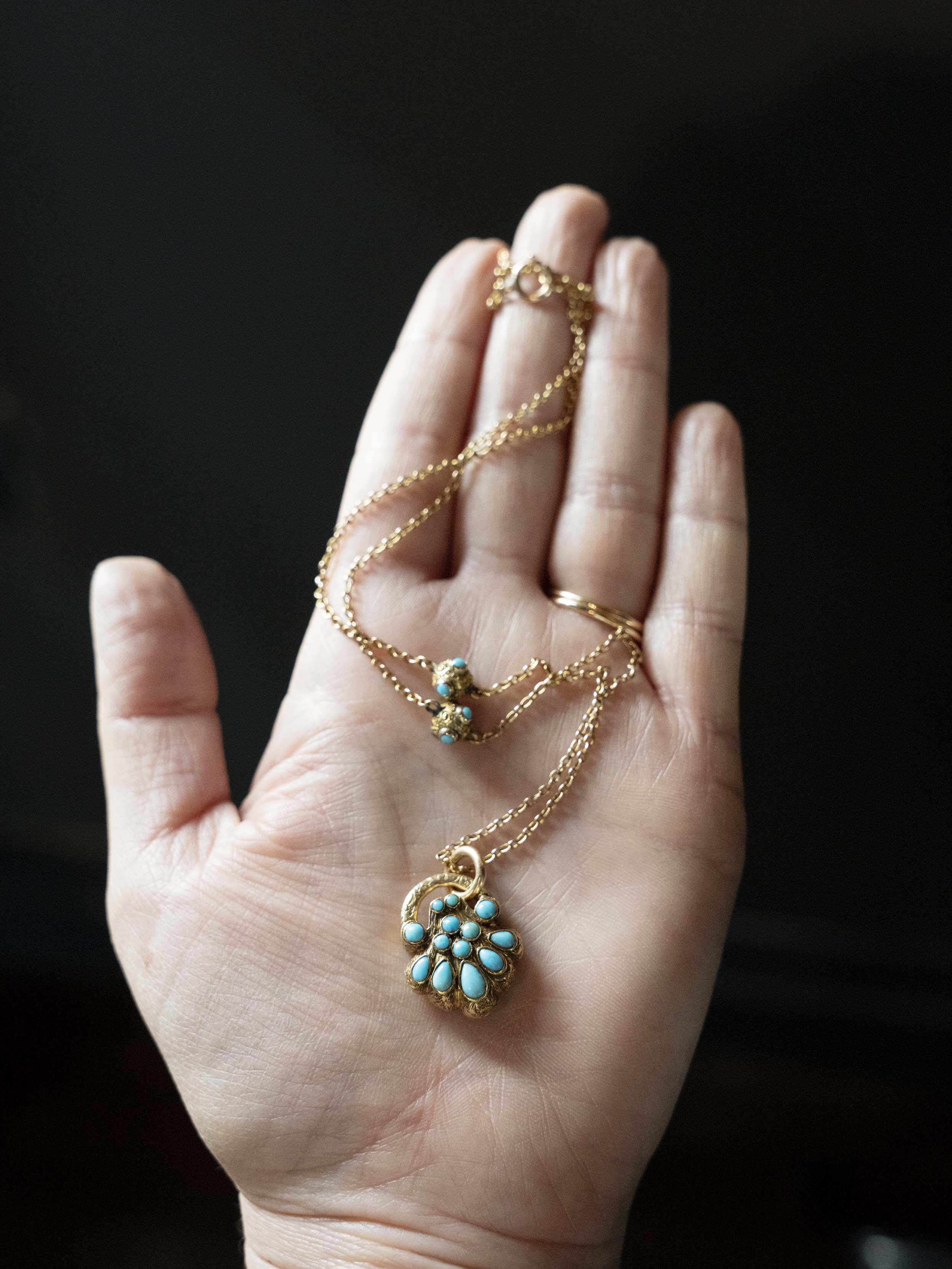 Early Victorian era turquoise padlock locket in 15k gold. It is in the form of a shell with Persian turquoise and a glazed compartment.&nbsp; English in origin. Circa 1840. Hanging on an antique 15k gold turquoise beaded ball chain. In the palm of someone's hand to show the scale of the piece. 