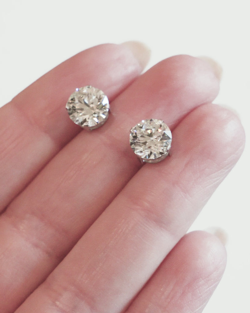 Classic round brilliant cut diamond earring studs. Handmade platinum four-tab prong settings with locking backs. Featuring two GIA certified diamonds, 2.01 carats J color and SI1 clarity and 2.01 I color and SI1 clarity. Over four carats in total weight. Front view of the diamond earrings.  A video of the earrings being held for a better view on the scale of them. 