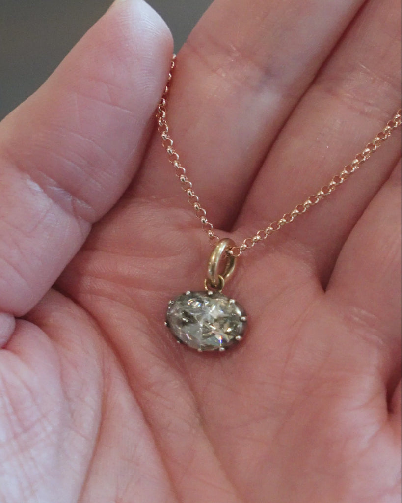 Georgian era rose cut diamond pendant necklace. The bright rose cut diamond is a subtle heart-shape, set in a foiled closed-back setting. Originally part of a larger piece of jewelry, it was later converted into a simple charm pendant. The diamond weighs approximately .95 carats. The diamond is quite flat and faces- up like a two-carat stone. Found in Paris. Circa 1820. Front view of the necklace. The diamond is hanging from a delicate gold chain. Video of the necklace in her hand. 
