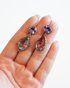 Lovely early 19th century earrings set in 15k gold. Cushion and pear shaped amethyst stones set in closed-back collet settings. The stones are a pale purple, with varied shades of purple and pink coming from the foil behind the stones. The coloring is very unique. English in origin. Circa 1800. Hand holding earrings for scale. 