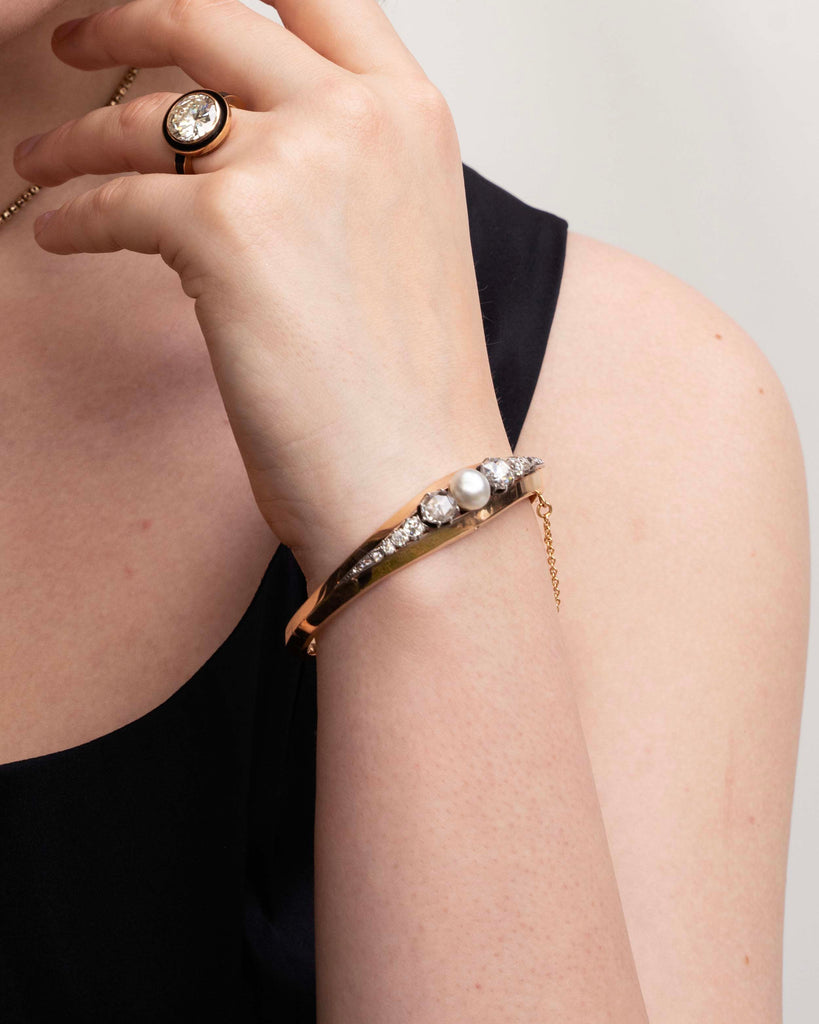 Approximately three carats of rose-cut diamonds are set in silver cut-away settings. The twenty diamonds flank a single natural pearl. The stones taper into a knife-edge detail in 18k rose gold. Continental Europe, circa 1860. Model wearing the bracelet with a diamond ring that has enamel details. 