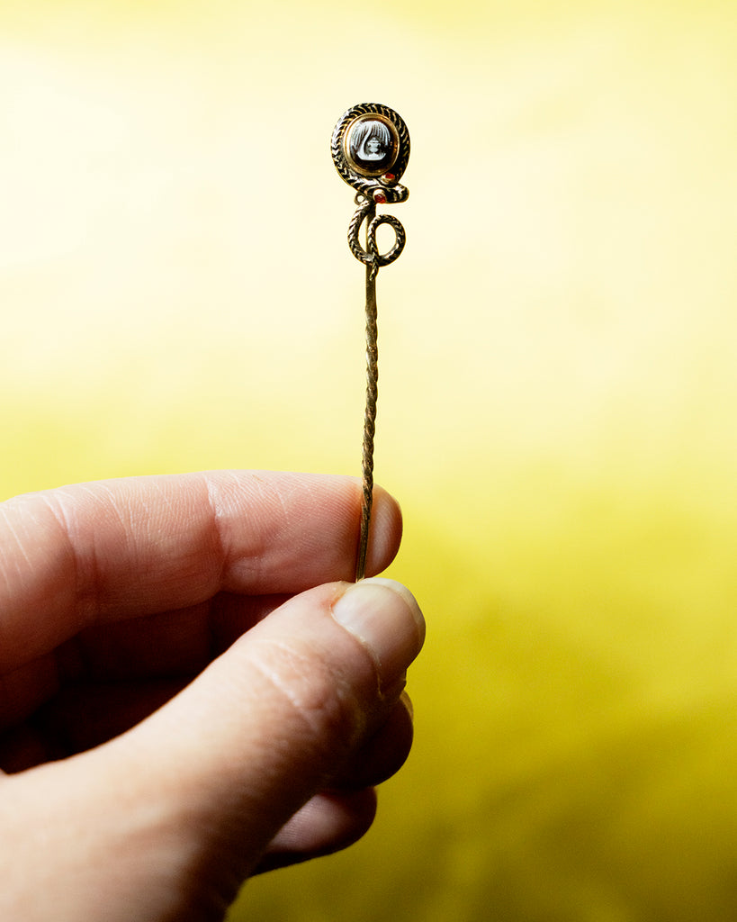 Early Victorian era mourning stick pin with enamel snake and carved hardstone urn, in gold. The mourning piece has engraved "H A& Levett ob March 12 1847". The original woven hair is the backside locket compartment.Can be worn as an accessory or displayed on the wall as a decorative piece. English in origin. Held in hand to show scale. 